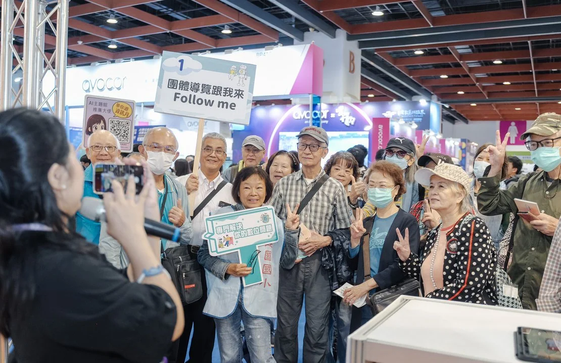 2025 現場實景：導覽團在展區前用手機記錄與合影