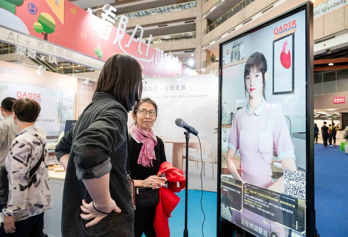 2025 現場實景：AI 主題館的 AI 擬真人互動螢幕前，民眾駐足體驗