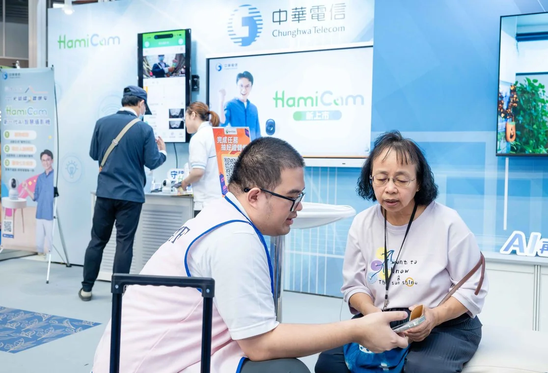 2025 現場實景：中華電信展區，工作人員協助長輩操作手機 AI 應用